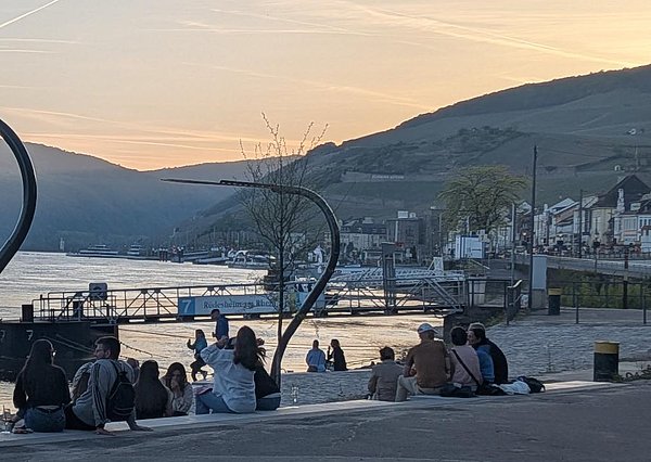 Goethestrand bei Sonnenuntergang. Menschen verweilen auf den Terrassen und schauen auf den Rhein. 